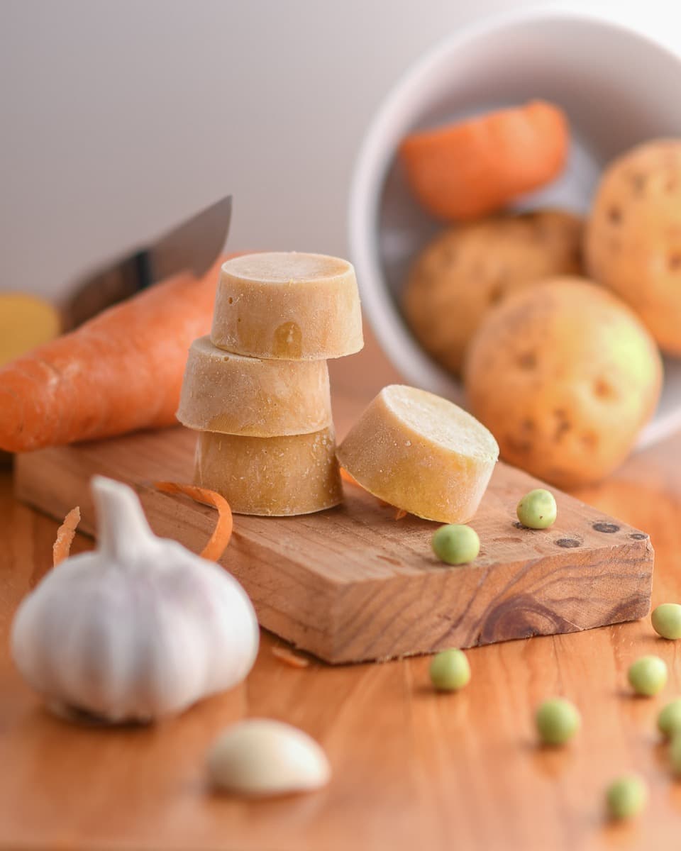 Moneditas ultracongeladas de sopita TUTUN sobre tabla con ingredientes frescos